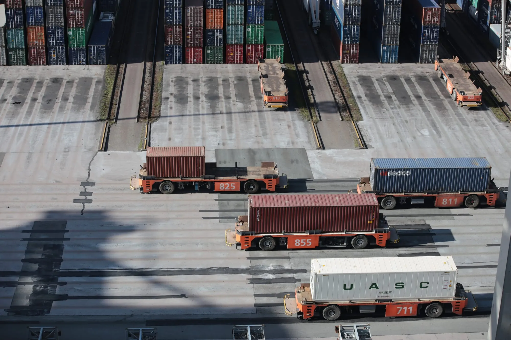 Container carriers moving between stacked containers at a port, seen from above